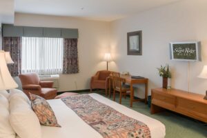 A Ridge Single King guest room, with one king bed dressed in white linen and a patterned runner, an armchair by the window, a writing desk and chair, a chest of drawers and a wall-mounted television