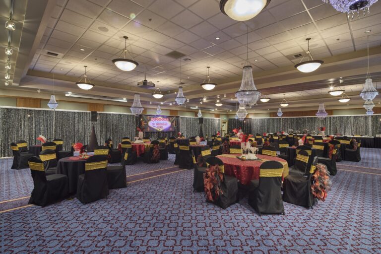 The ballroom laid out for an event, banquet rounds and a staged backdrop beneath chandeliers