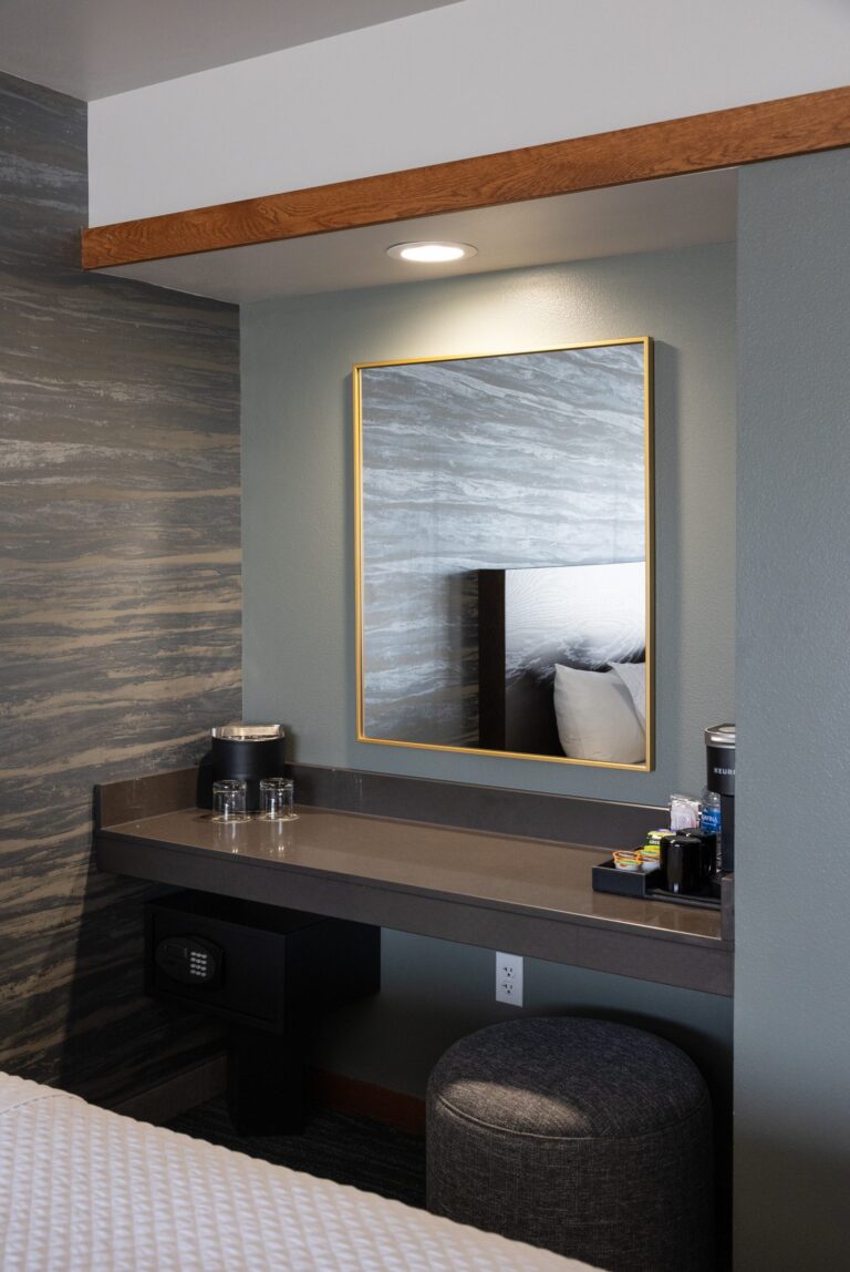 The vanity in a Double Queen room, a gold-framed mirror above a dark counter with a round stool
