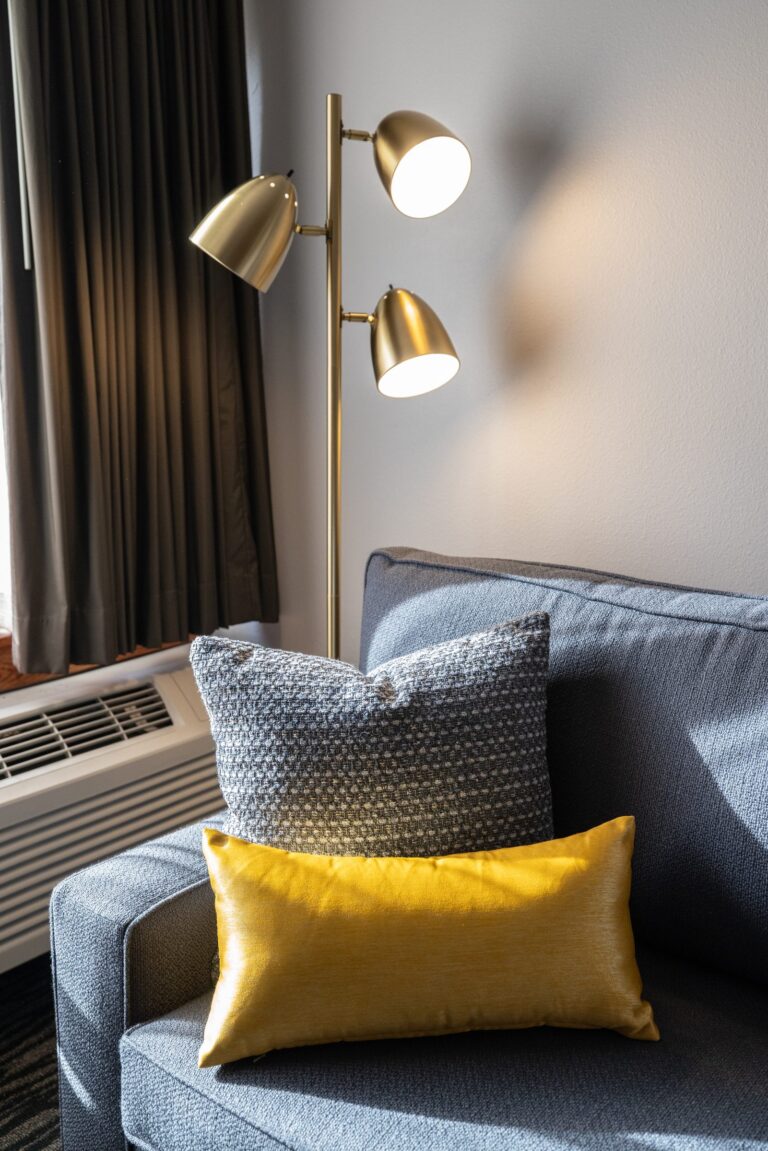 A grey sofa with a gold cushion beneath a brass wall light in the King Suite