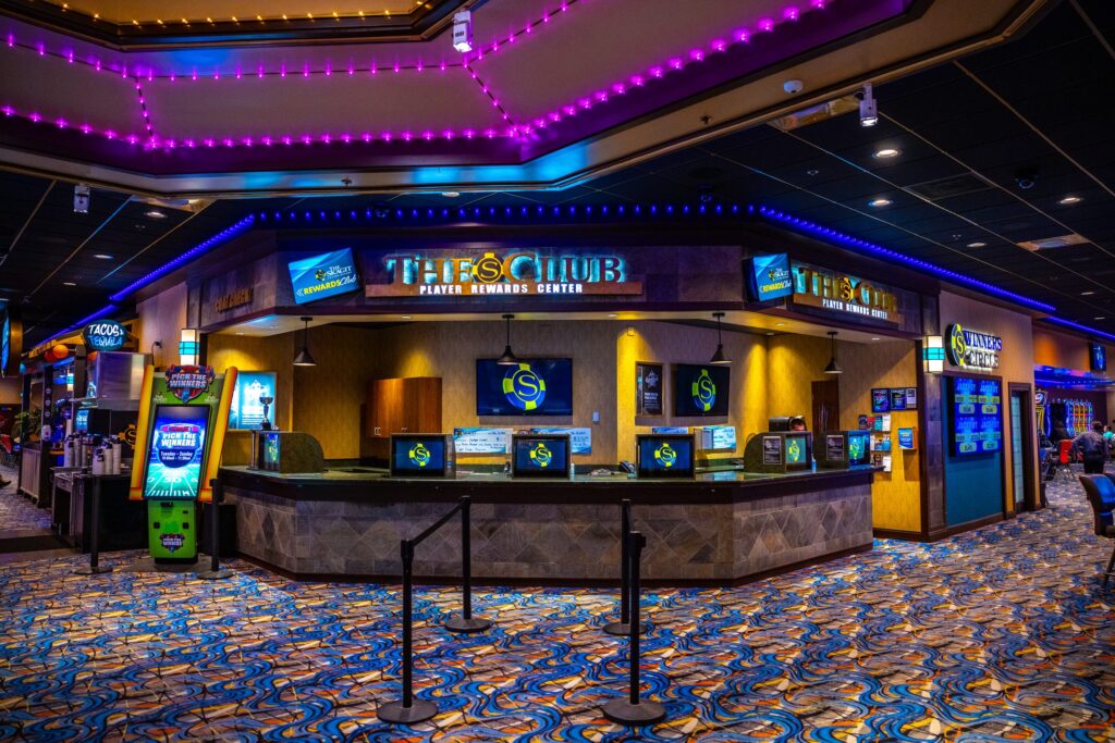 The S Club Player Rewards Center desk on the casino floor, staffed counter beneath a lit sign and screens