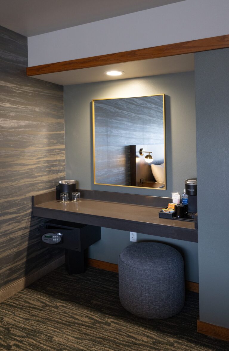 The vanity area of a Single King room, a lit mirror above a dark counter with a padded stool